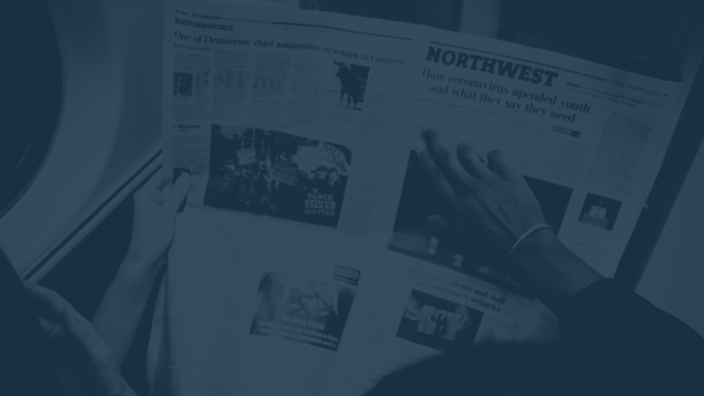 A photo of two people reading through a newspaper with navy blue overlay.